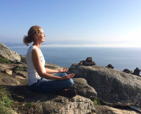 Anni sidder i meditativ stilling på en klippeafsats over havet